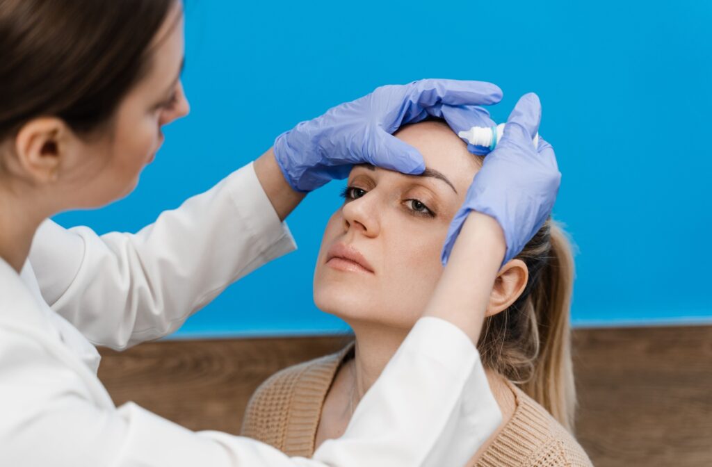 Eye doctor drips eye drops into eyes of female patient to treat Meibomian Gland Dysfunction (MGD)