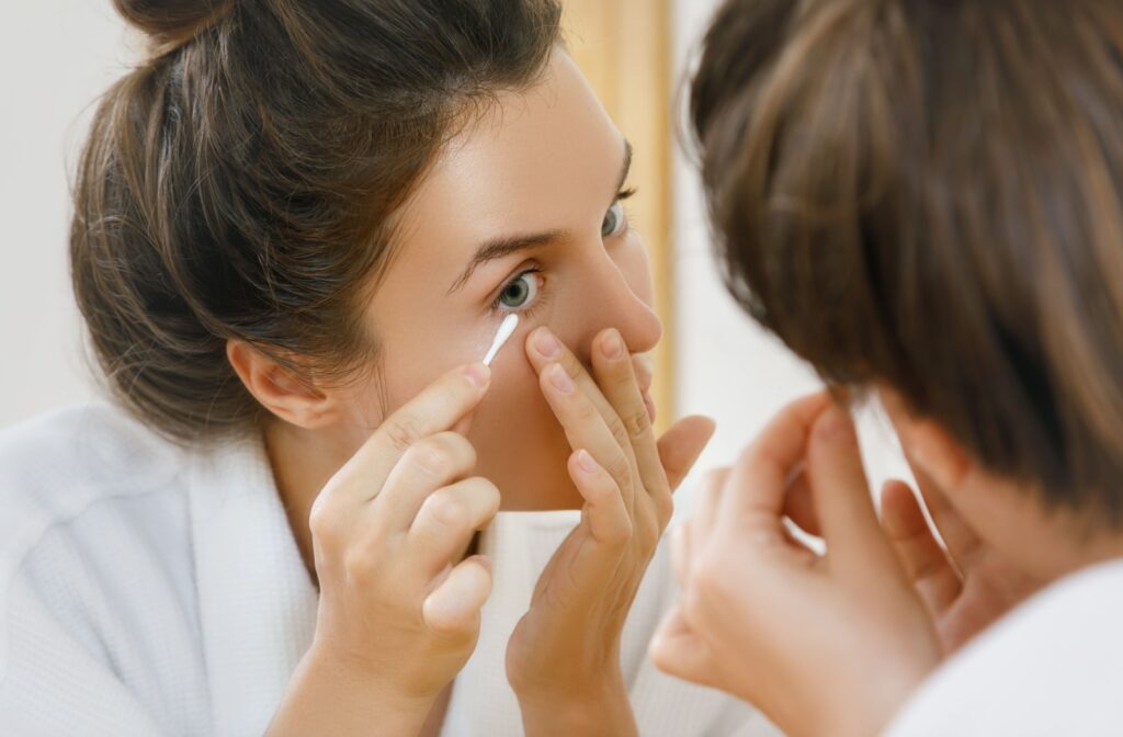 A woman cleaning her eye with a cotton swab to benefit her eyelid hygiene and avoid meibomian gland dysfunction.