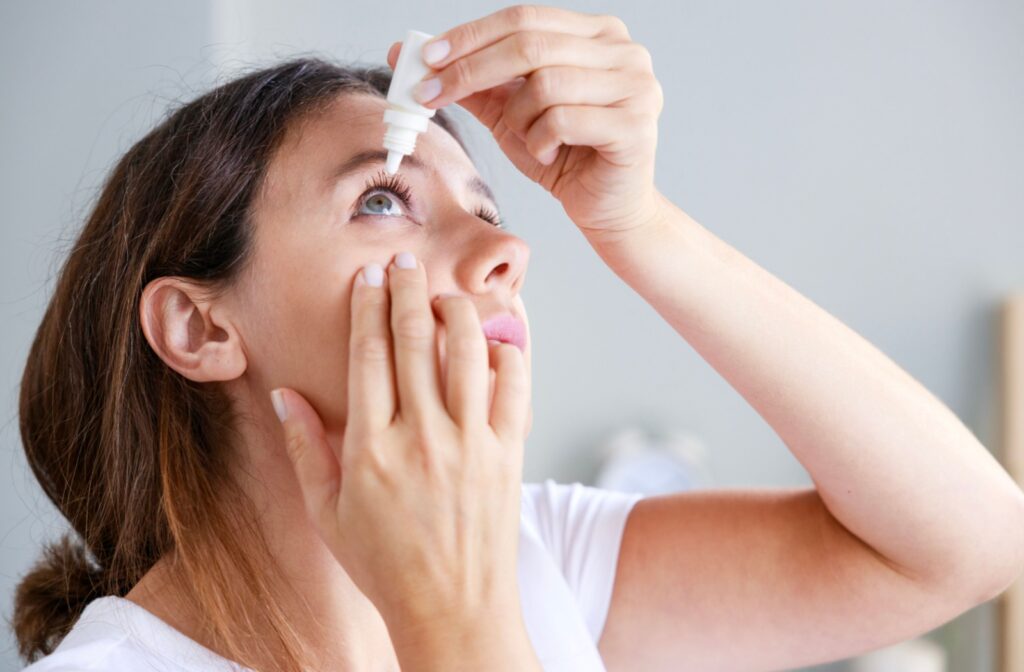 A woman gently pulls down on her face as she drips eye drops into her eye.