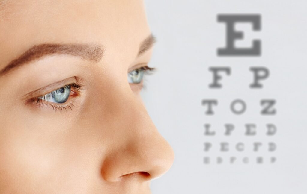 A person's upper face is shown to the left while a slightly blurred Snellen Eye Chart is shown to the right