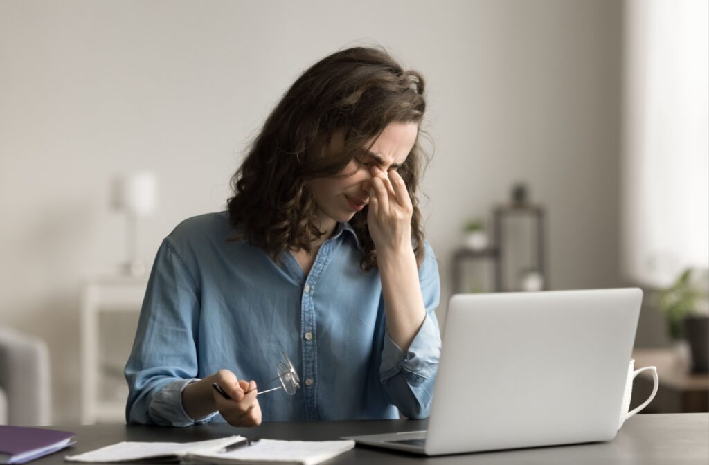 Woman sitting in front of a laptop pinching in between her eyebrows