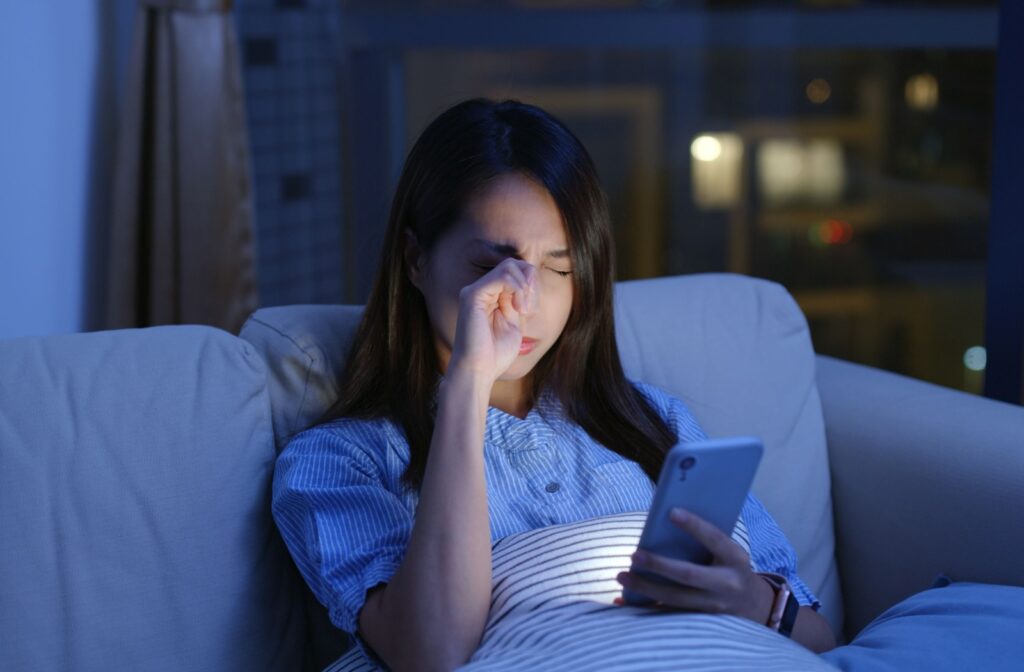 Person rubbing their eyes as they use their phone in the night