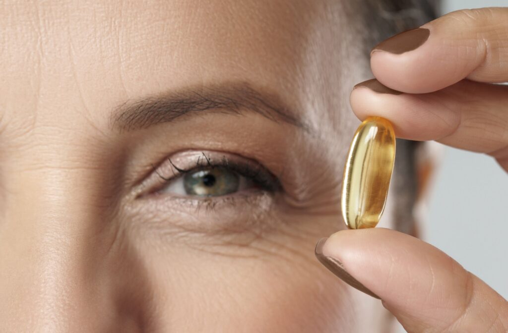 A close up of a person holding an omega-3 vitamin next to their dry eye